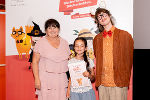 Zwei Personen, eine ältere und eine jüngere, stehen lächelnd vor einem Banner mit dem Aufdruck "Bücherhelden". Die jüngere Person hält eine Urkunde.