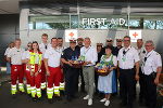 Gruppe in Uniformen vor einem Gebäude mit dem Aufdruck 'FIRST AID'. Jausenkörbe werden überreicht.